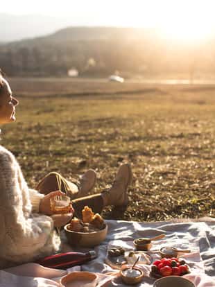 Back view of young woman relaxing and enjoying sunset in autumn. Happy beautiful girl on the nature picnic - camping. Cozy autumn outdoor concept.