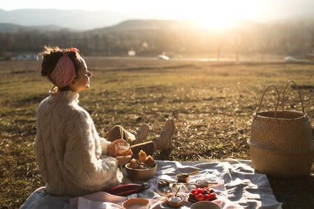 Back view of young woman relaxing and enjoying sunset in autumn. Happy beautiful girl on the nature picnic - camping. Cozy autumn outdoor concept.