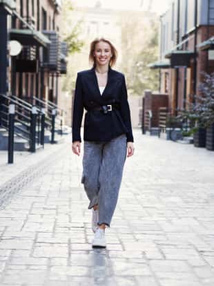 Confident Businesswoman or fashion blogger In Stylish Office Clothes walking city street. Beautiful Smiling Woman Going To Work, Wearing Style Fashionable Spring or fall black jacket, oversize slouchy jeans. Outdoors. Autumn trend