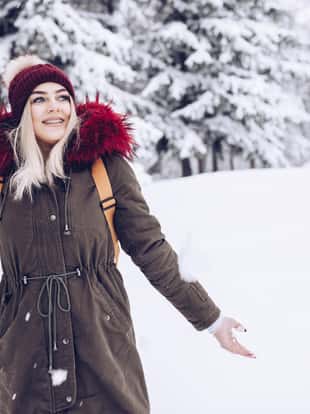 Snowy day, female hiker is enjoying her day in the nature, warm clothing and knitted hat