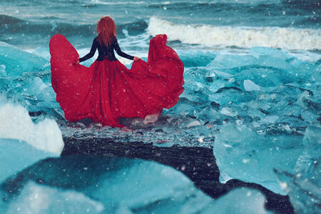 rear view of fashion model in flying red dress in the ice posing in snowy day.photo taken on Diamond Beach in Iceland.