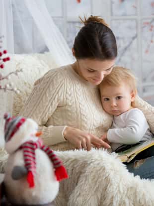 Mother breastfeeding her toddler son sitting in cozy armchair, snowing outside wintertime