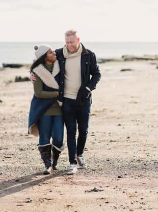 Mid-adult mixed race couple walking on the beach and laughing.