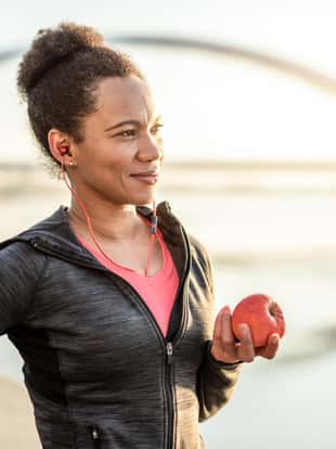 Happy African American Athletic Woman Eating An Apple After Exercise.