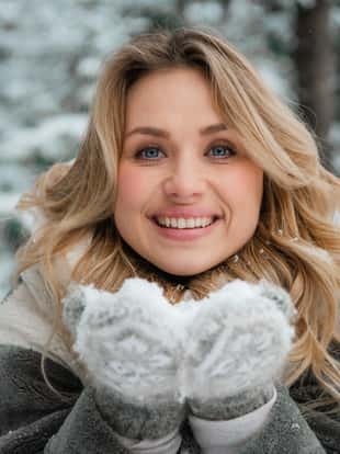 Winter portrait of a beautiful russian blonde girl with long hair standing in a snowfall in the forest