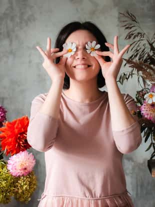 woman professional florist with humor poses with flowers eyes sitting wooden table with compositions wild flowers. Flower shop. Background, concrete. Concept inspiration, floral, greetings, spring
