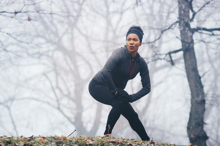 A woman warming up for exercise on a misty morning in nature. She is stretching her legs. She wears ear phones. Full view, lower view.