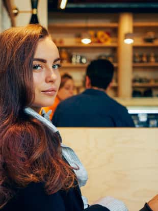 Portrait of a young attractive woman with beautiful chestnut hair who is sitting in a coffee shop while waiting for her morning coffee