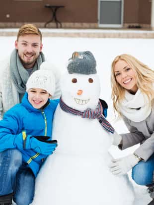 Beautiful smiling family making family portrait with their pet rertriever and snowman in back yard of the house