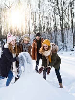 Group of young friends outside in winter, building a snowman.