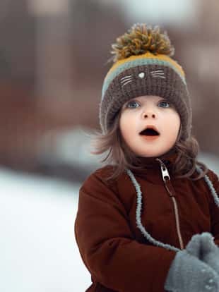 Baby girl of 2-3 years old in the garden in winter time, standing and looking away with mouth open, surprised and shocked