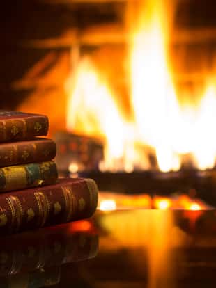 Antique books in front of warm fireplace. Magical relaxed cozy atmosphere near fire.