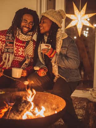 Couple enjoy in winter night at porch, they preparing marshmallow, enjoy in warmth of fireplace and coffee