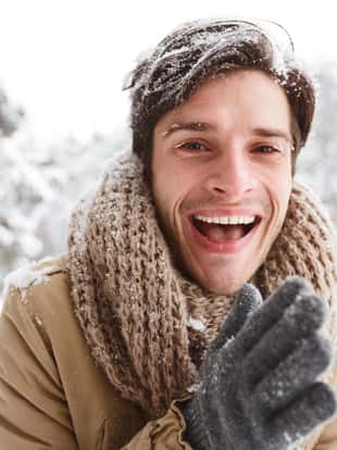 Cheerful Guy With Snow In Hair Rubbing Hands To Warm Up Smiling At Camera Standing In Winter Forest