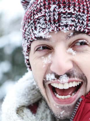 Lachender Mann mit Schnee im Gesicht im Winter