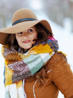 pensive modern female in brown hat and scarf outdoors in the city park in winter in sheepskin coat.