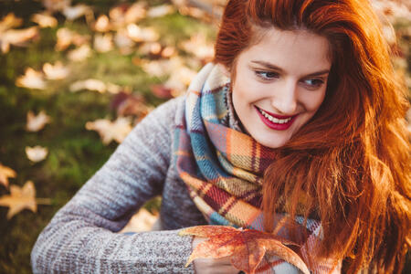 Portrait of redhead woman, holding leaves. Sitting in park, and enjoying in autumn.