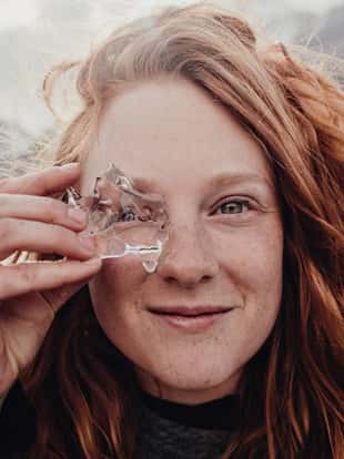 Red haired Girl looking through glacier ice in mountain backdrop on trip to el cheltan Argentina patagonia