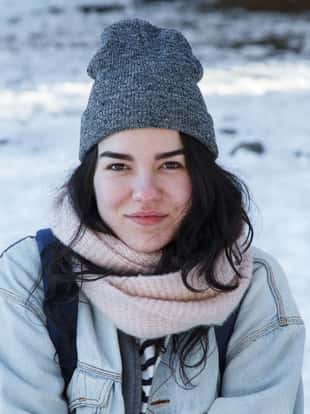 Young caucasian white woman with brown eyes wearing a cap and warm clothes in the snow. She enjoys a winter vacation trip in the snowy forest.