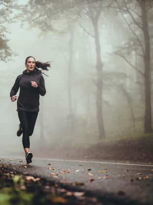 Determined athletic woman running through misty nature. Copy space.