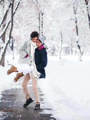Young man is piggybacking his girlfriend in snowy public park.