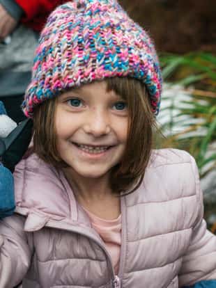 Young girl wearing a colourful beanie, smiling and about to throw a snow ball