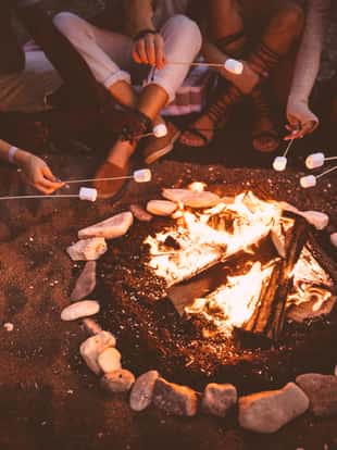 Close-up of young multi-ethnic hipster friends' hands roasting marshmallows over bonfire on camping trip