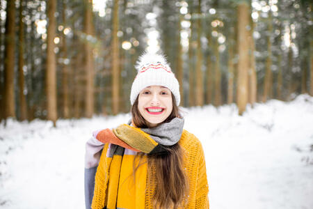 Portrait of a young woman dressed in bright winter clothes standing in pine forest during the winter time