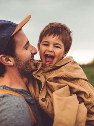 Photo of father and son spending time in the nature together. Boy is covered in father's jacket since he's getting cold.