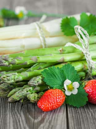 Fresh green and white asparagus with strawberries on wooden background
