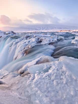 Godafoss frozen waterfall during Winter at sunrise. North Iceland.