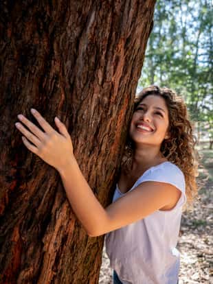 Portrait of a very happy woman hugging a tree at the park and enjoying nature