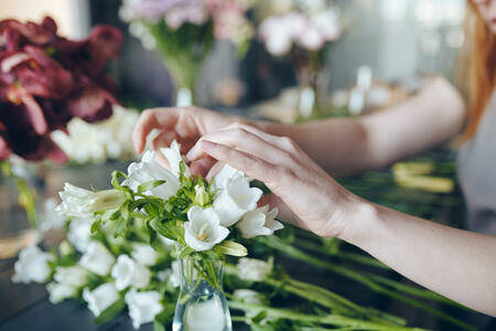 Close-up of unrecognizable woman adjusting white flowers in vase while making bouquet in flower shop
