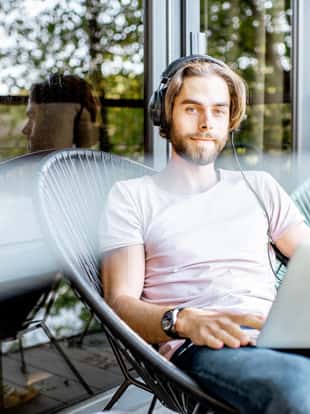 Poortrait of a handsome man working with laptop and headphones on the balcony of the house in the beautiful green forest