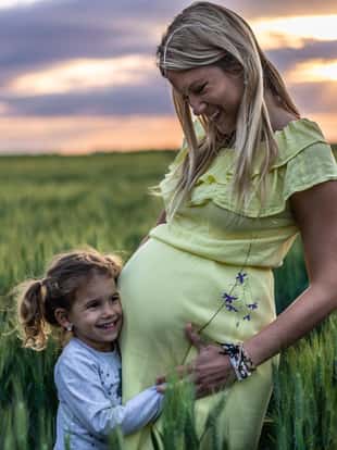Young pregnant mother spending time with her daughter in nature on a sunset.
