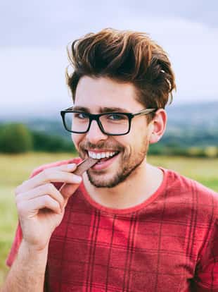 Teenage boy eating chocolate while standing in the meadow.