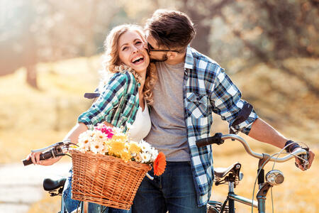 Trendy young couple stop to riding on their bike with basket of flowers while focused on hug.