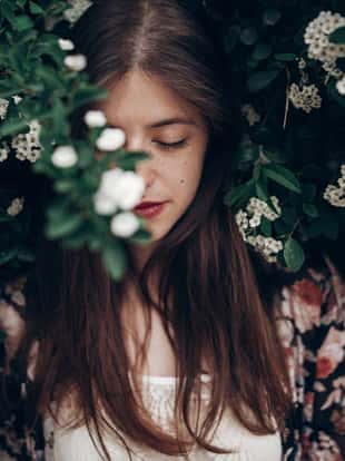 calm portrait of beautiful hipster woman in blooming bush with white flowers of spirea. boho girl sensual portrait in floral modern clothes in greenery. space for text