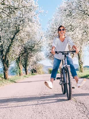 Happy smiling woman rides a bicycle on the country road under the apple blossom trees