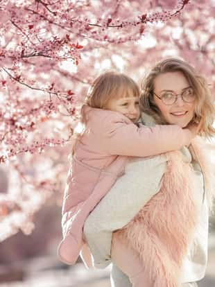 Mom hugs baby on walk in garden. Family mother and daughter among trees with flowers in blossoming period