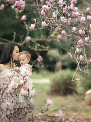 Young mother and little daughter in autumn park play with Japanse magnolia leaves. Happy weekend with family in autumnal forest park. People in park. Smiling woman and baby in outdoor. Fall. Sunny day