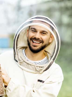 Portrait of a cheerful beekeeper in protective uniform with bee smoker on the apiary