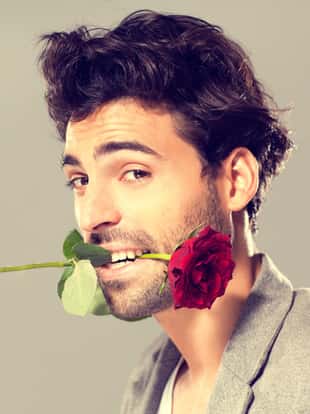 Close up of a young man with red rose in his mouth.