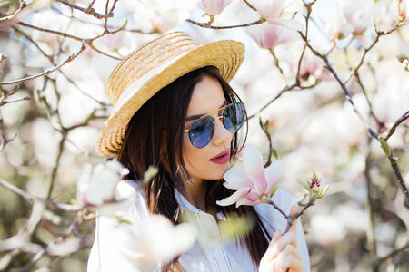 Young woman in hat and sunglasses surrounded with magnolia flowers tree