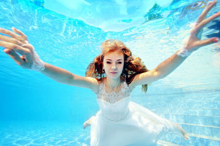 Bride in white dress swims underwater toward the camera. Portrait. Close-up. Horizontal orientation. A view from under the water