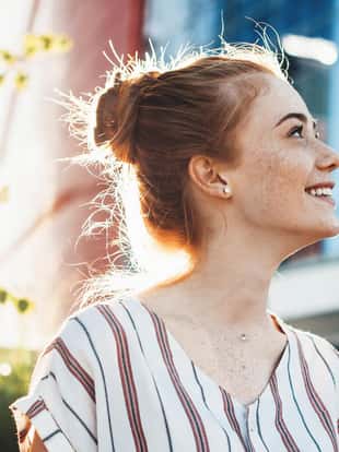 Cheerful young woman with freckles and red hair posing against the sunshine and smile looking up