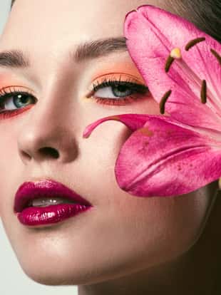 close-up portrait of beautiful young woman with stylish makeup and pink lilium flowers isolated on white
