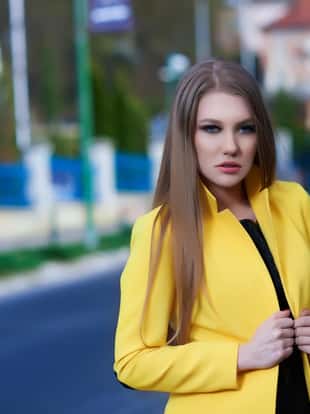 fashion woman posing outdoors, yellow jacket and intense look. photo taken in beautiful summer day.