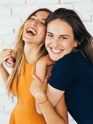 Two friends dancing and having fun in front of a white brick wall.