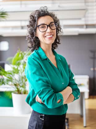 Portrait of happy mature businesswoman standing with her arms crossed. Mid adult female looking at camera and smiling while standing in office.
